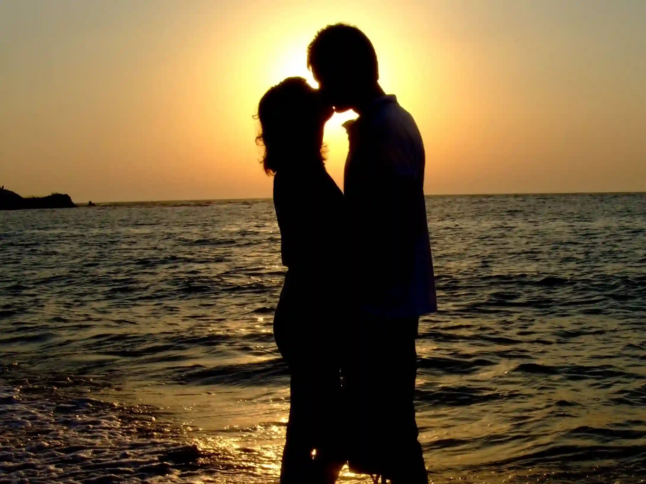 Silhouetted couple sharing a romantic moment at sunset by the sea