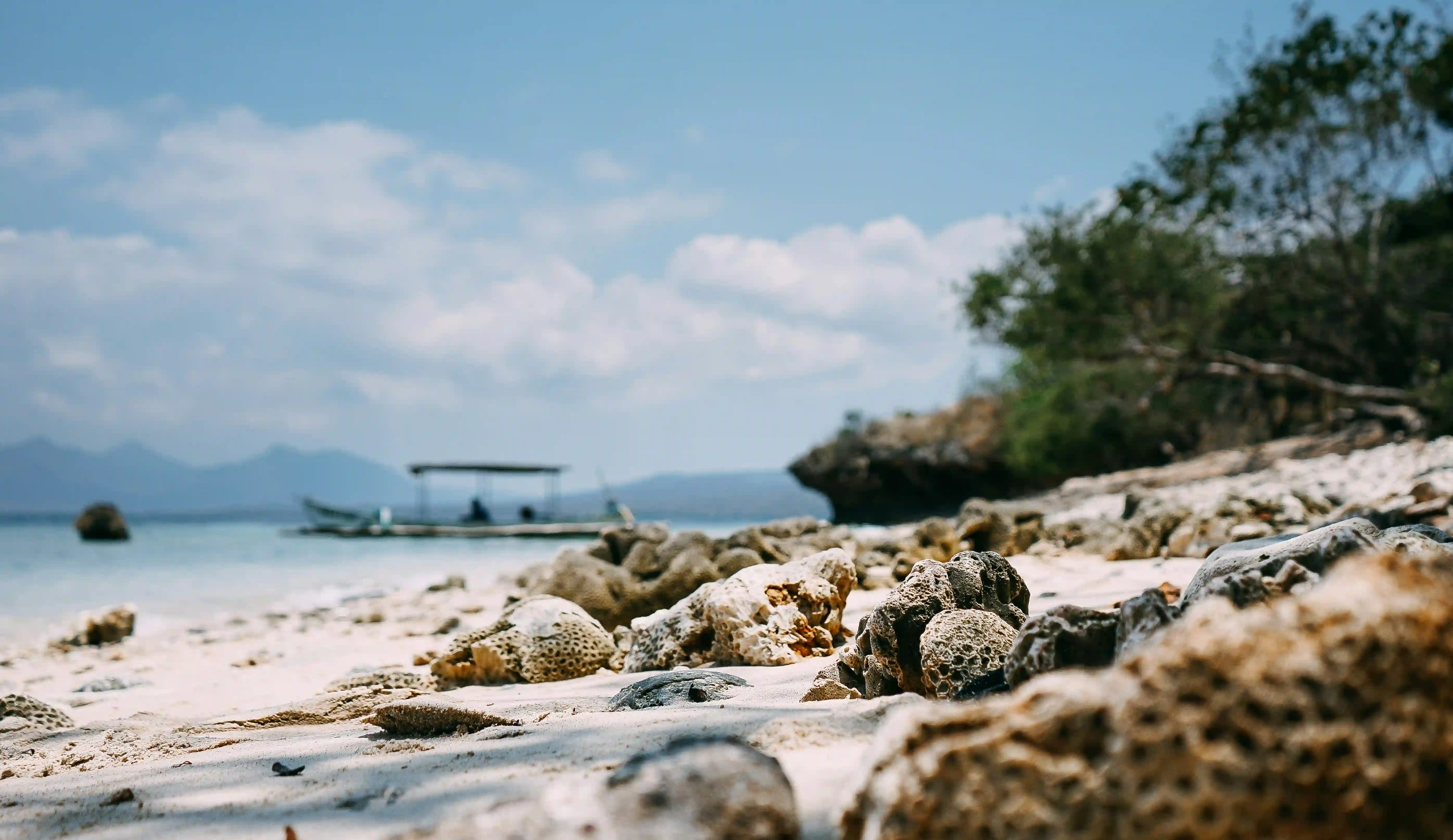 Remote white sand and rocky beach on Menjangan Island with a boat anchored nearby.