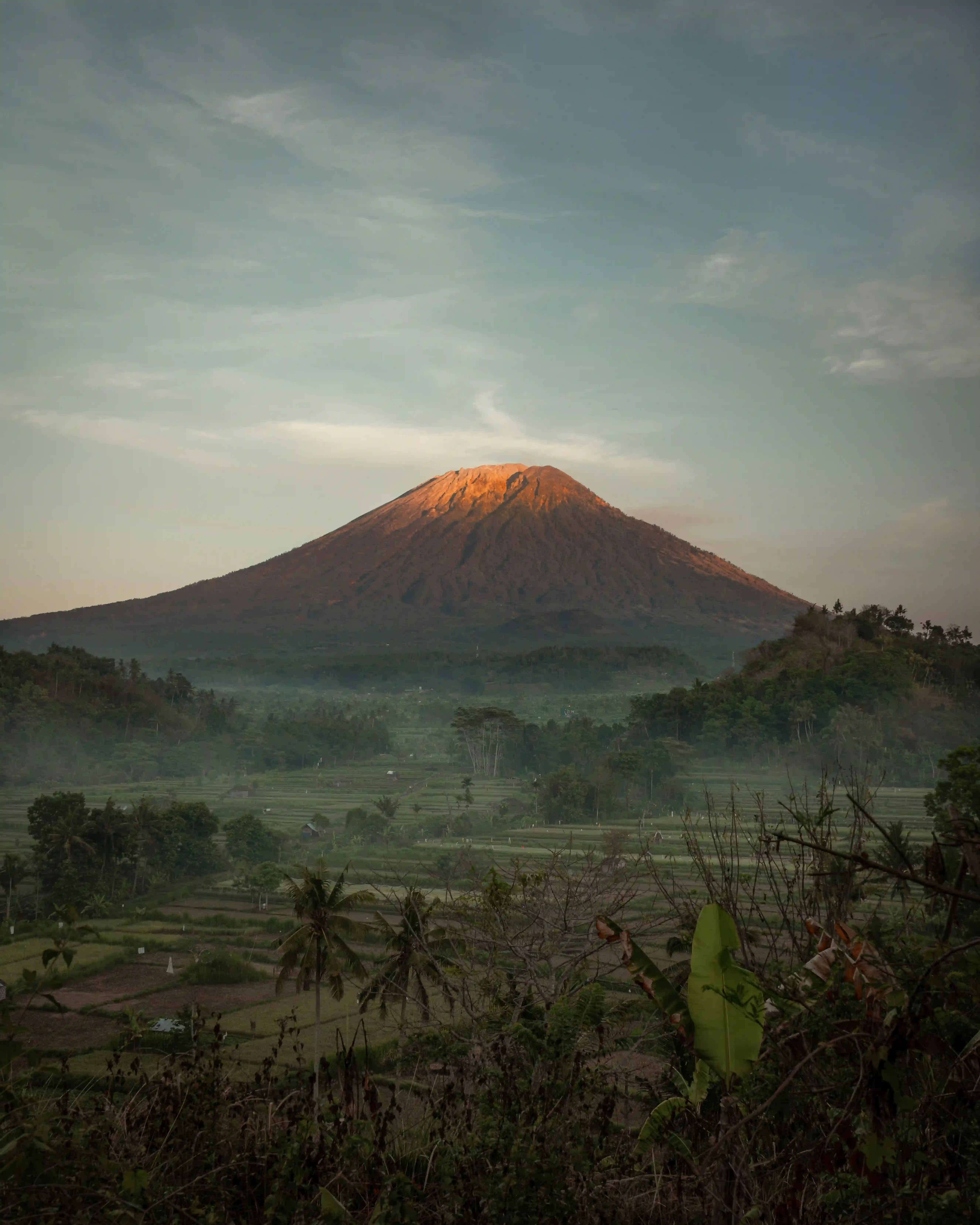 Majestic Mount Agung volcano at sunrise with golden light over rice fields.