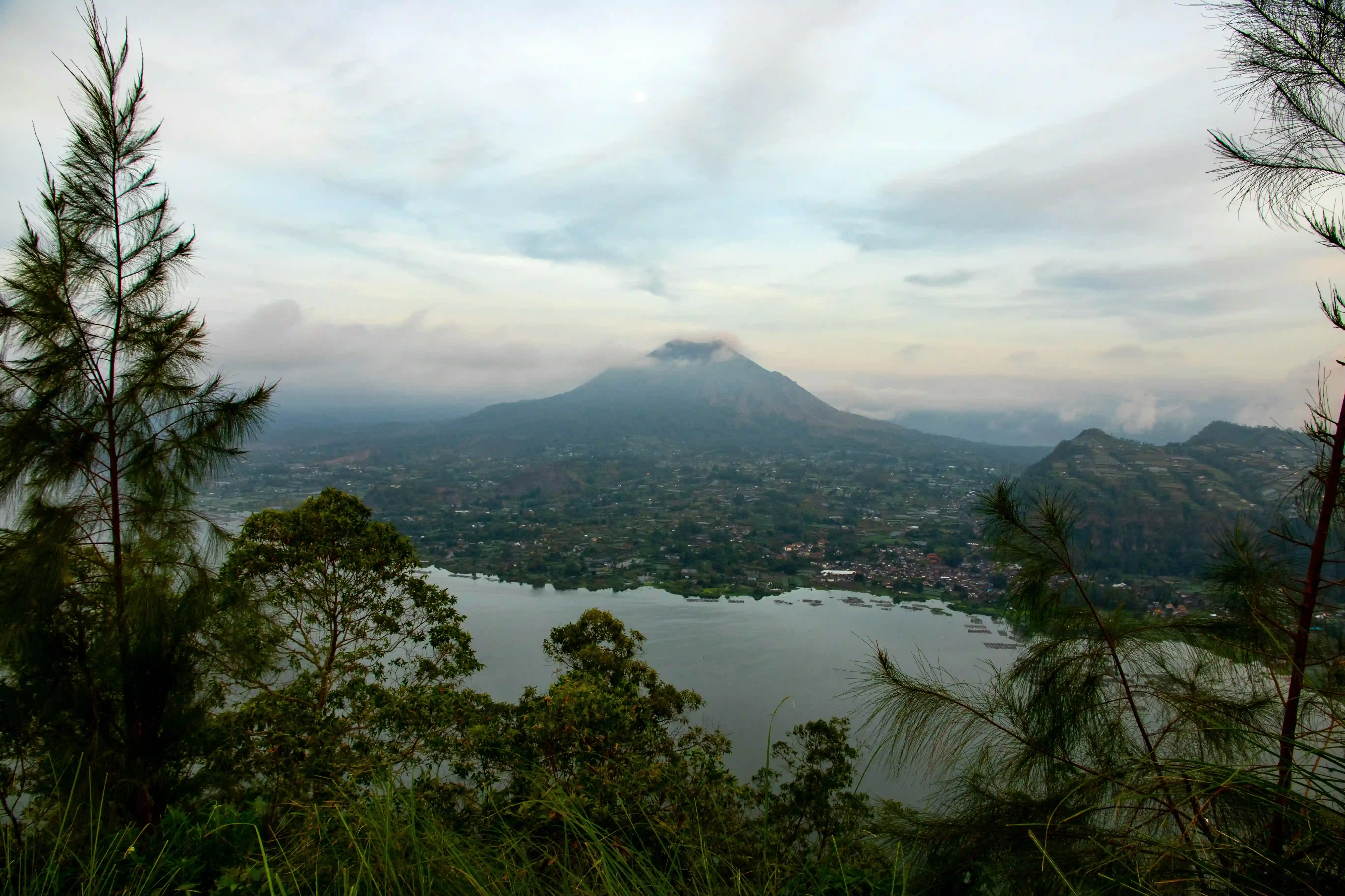 View of Mount Batur volcano and Lake Batur under a cloudy sky.