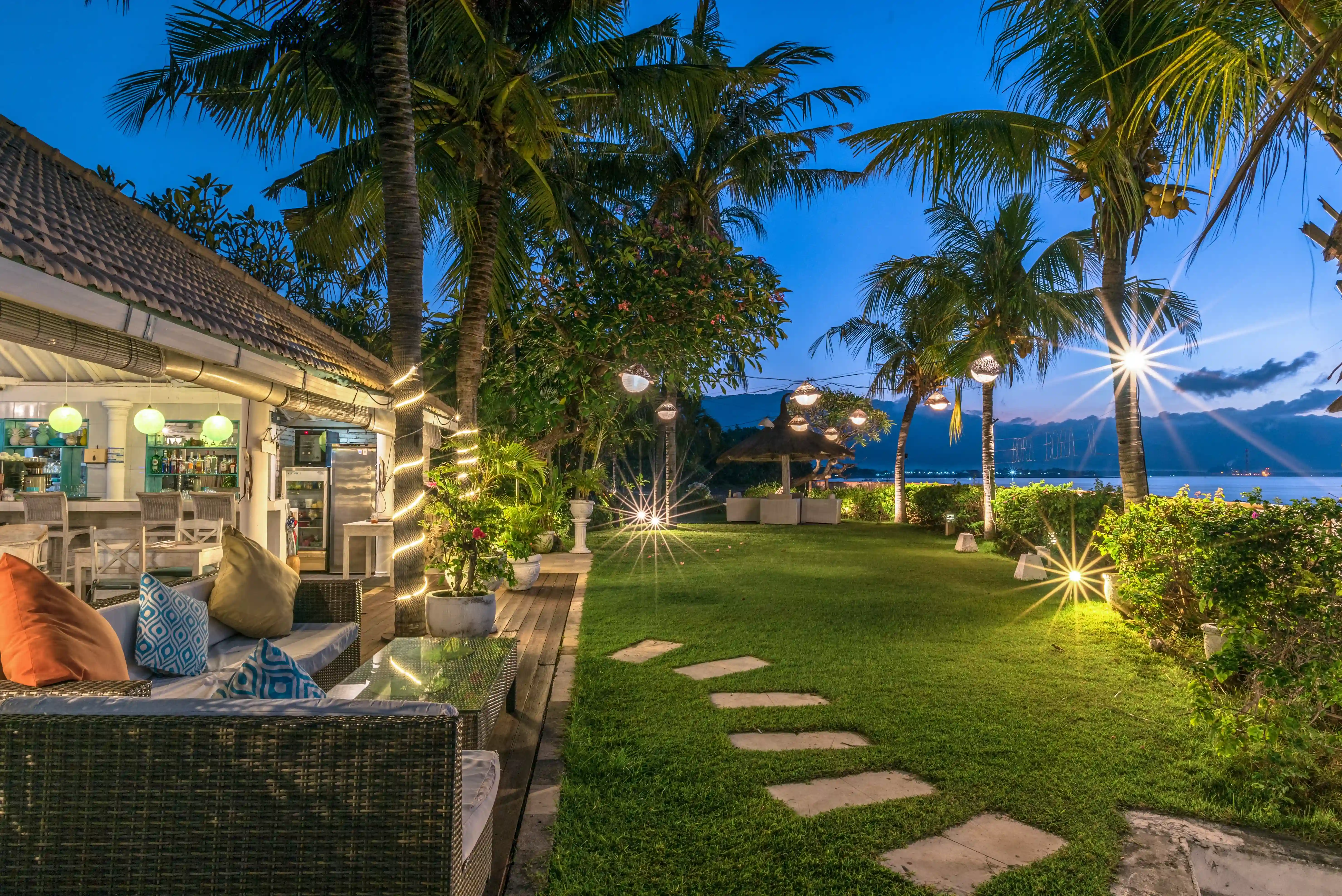 Exterior view of the illuminated resort lounge and bar area at night, surrounded by palm trees and string lights.