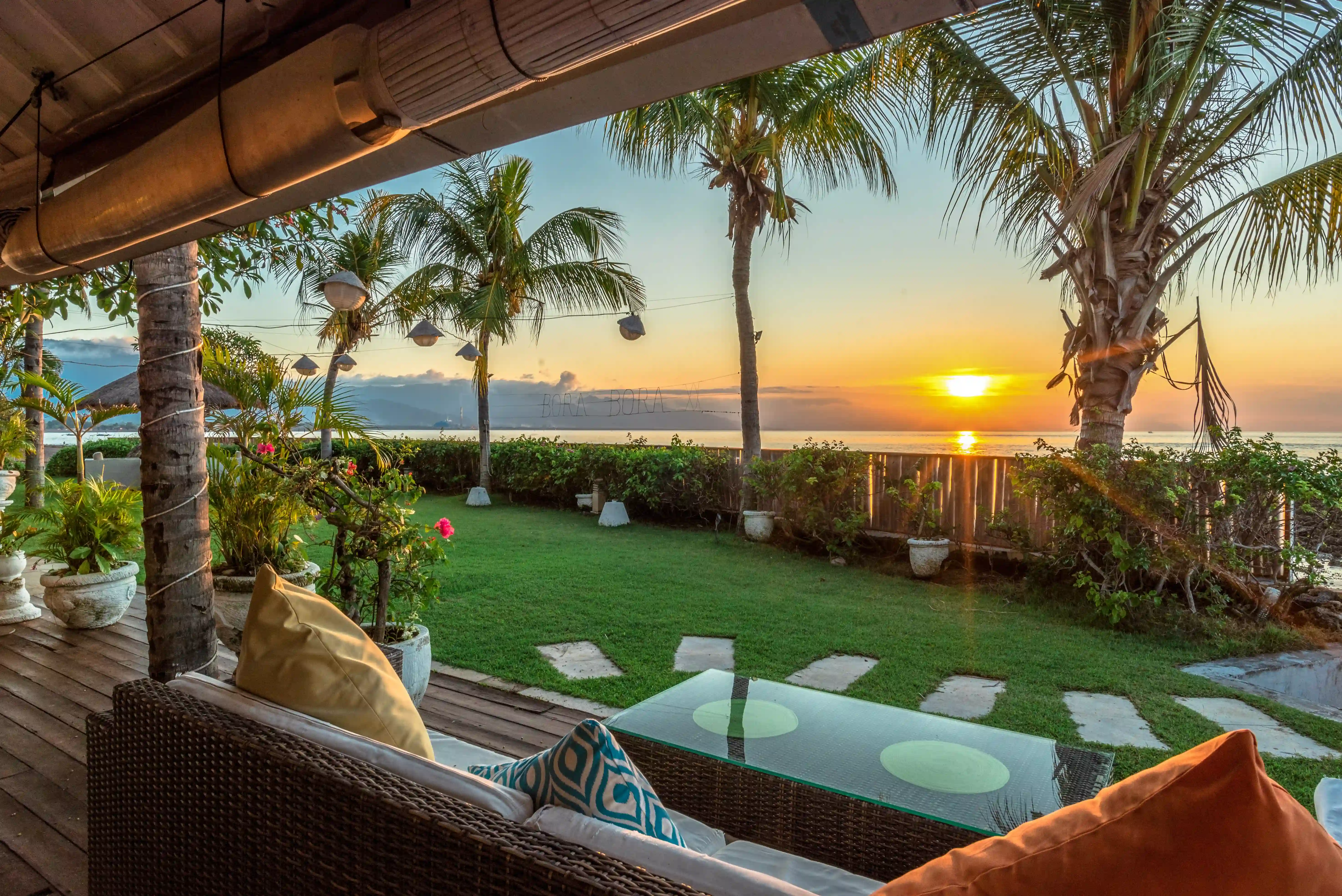 Lounge seating on the restaurant's deck, offering a view of the sunset over the water and palm trees.