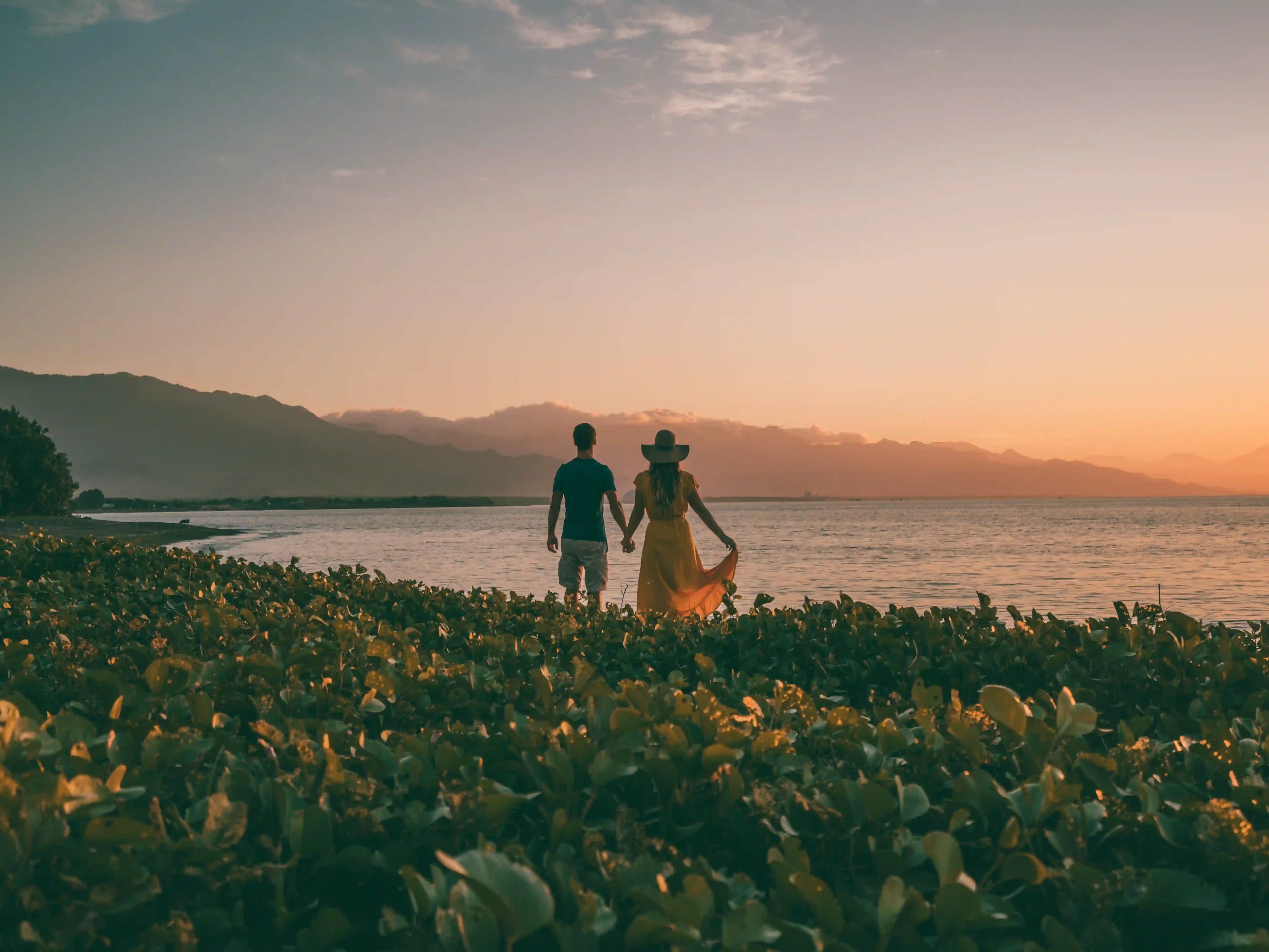 Romantic couple holding hands, watching the sunset on a Bali beach.