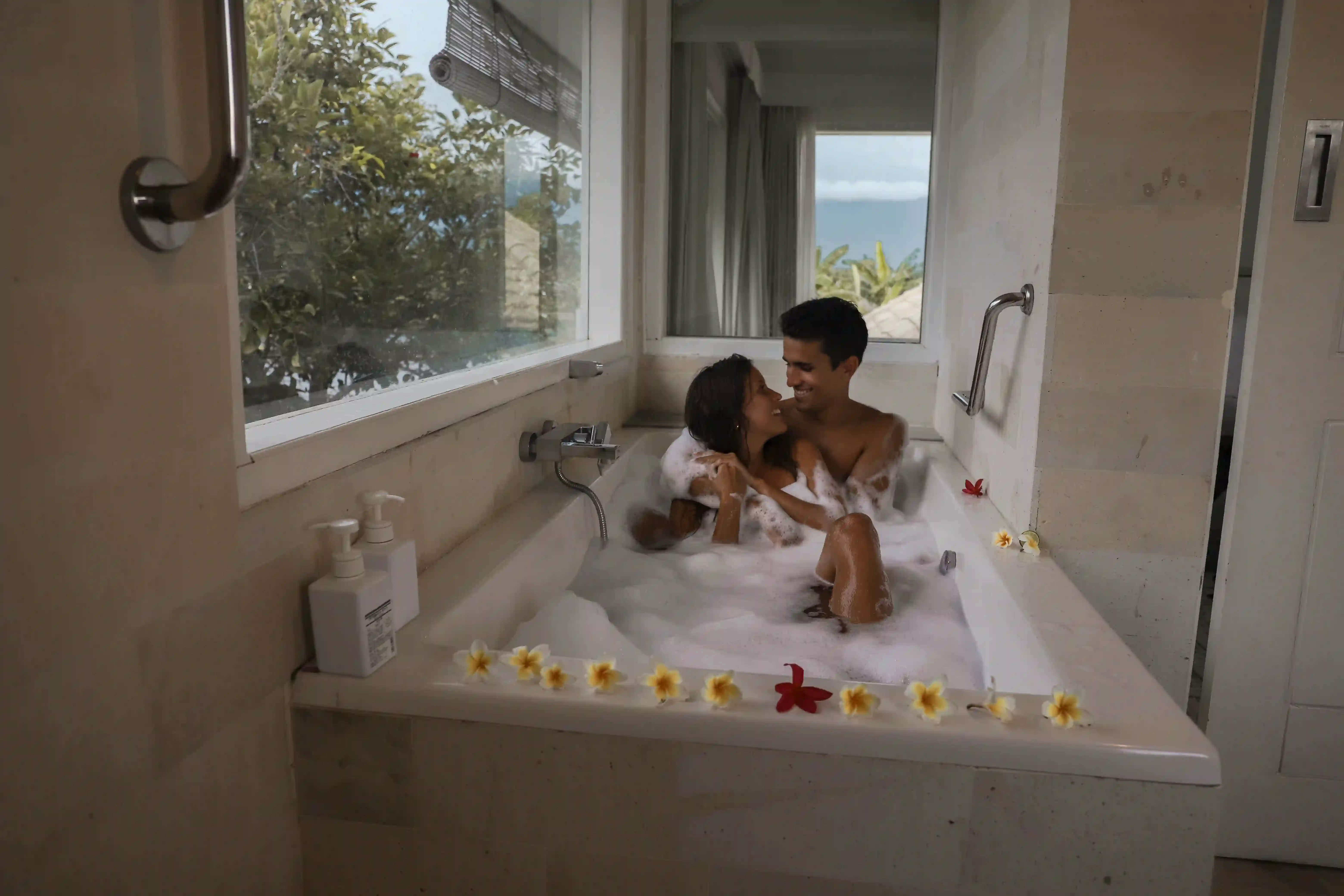 Romantic couple relaxing in a bubble bath in a luxury resort bathroom decorated with flowers