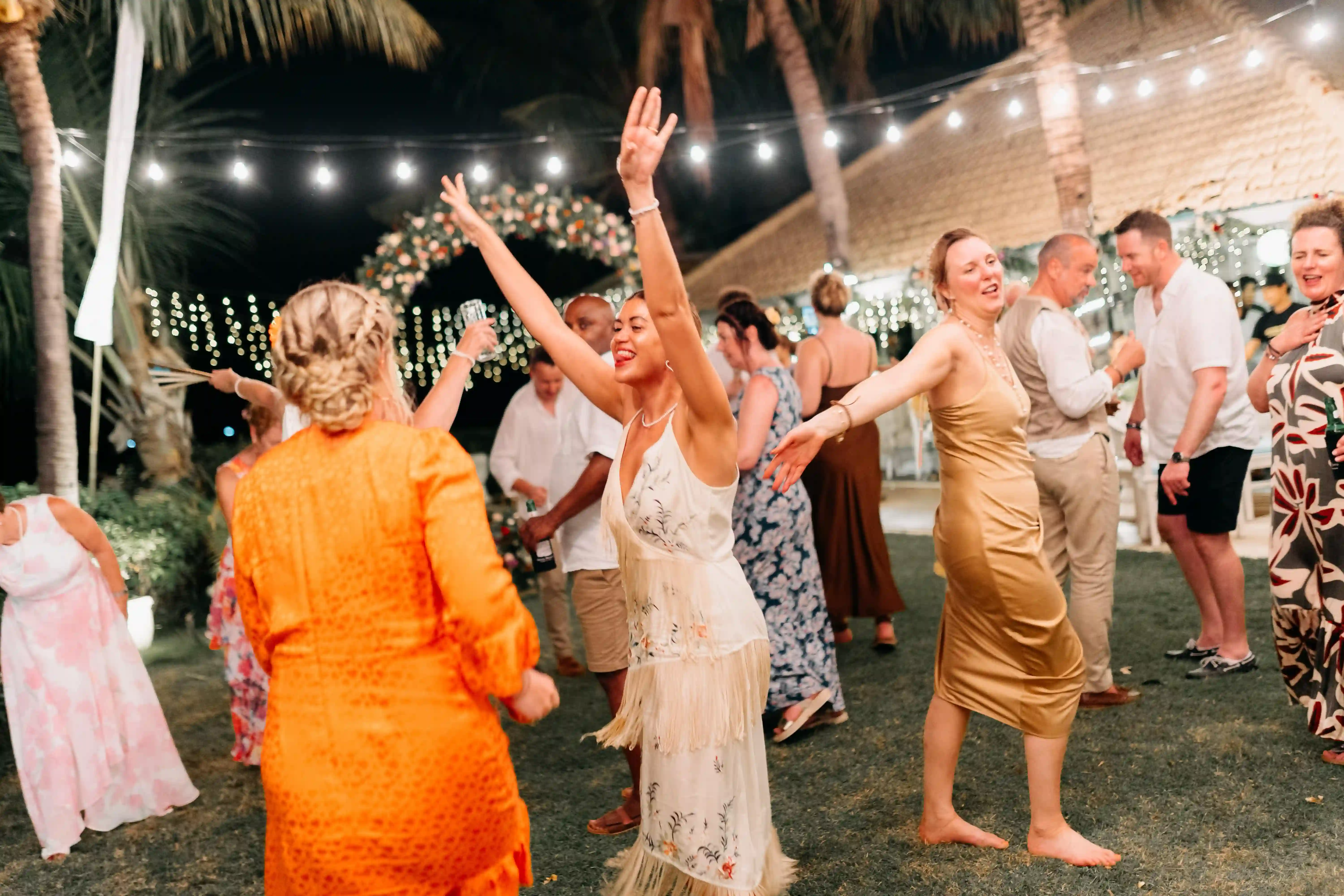 Wedding guests dancing and celebrating at a night-time reception with string lights.